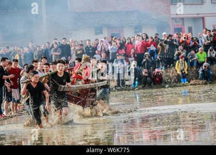 Chinese villagers of the Hakka people carrying a golden statue of ancient Chinese general Guan Gong dash through waterlogged fields during a mud-spatt Stock Photo