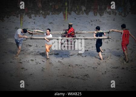 Chinese villagers of the Hakka people carrying a golden statue of ancient Chinese general Guan Gong dash through waterlogged fields during a mud-spatt Stock Photo