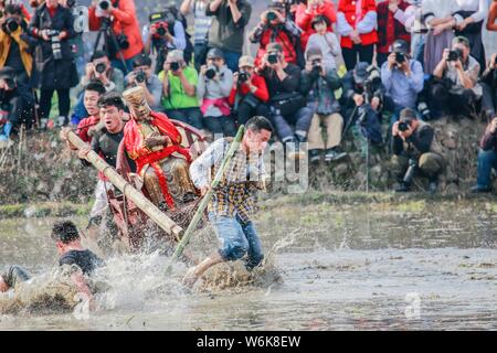 Chinese villagers of the Hakka people carrying a golden statue of ancient Chinese general Guan Gong dash through waterlogged fields during a mud-spatt Stock Photo