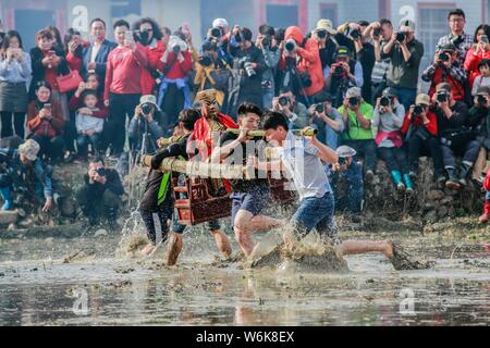 Chinese villagers of the Hakka people carrying a golden statue of ancient Chinese general Guan Gong dash through waterlogged fields during a mud-spatt Stock Photo