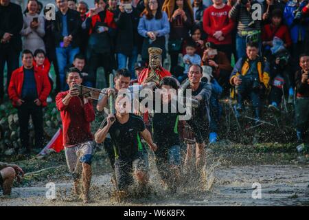 Chinese villagers of the Hakka people carrying a golden statue of ancient Chinese general Guan Gong dash through waterlogged fields during a mud-spatt Stock Photo