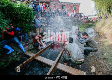 Chinese villagers of the Hakka people carry a golden statue of ancient Chinese general Guan Gong down to a river and splash water on the statue to cle Stock Photo