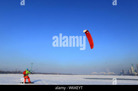 A snowkiter uses a large kite to glide on snow in Harbin city, northeast China's Heilongjiang province, 4 January 2018.      Snowkiting or Kite skiing Stock Photo