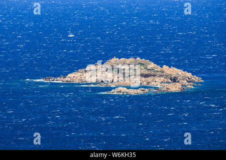 View from above, stunning aerial view of a rough sea with a small rocky island and a sailboat in the background. Sardinia, Italy.