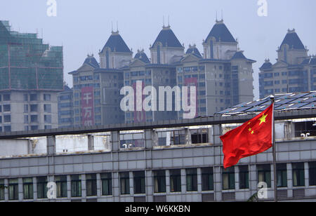 --FILE--A Chinese national flag flutters in front of high-rise buildings of a residential property project under construction in Ji'nan city, east Chi Stock Photo