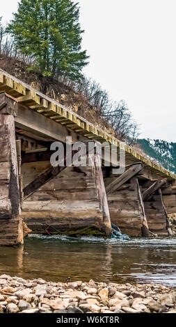 Vertical frame Rustic wooden bridge over a rocky stream with shiny water Stock Photo