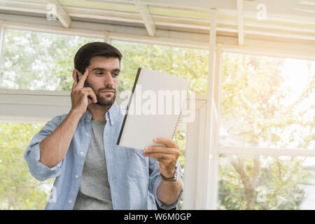Handsome man have beards wear gray t-shirt and wear a blue shirt over the outside, wearing wrist watch in hand holding a notebook and pen, are using t Stock Photo