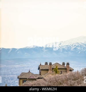 Square frame Homes and brown leafless trees on a hill blanketed with snow during winter Stock Photo