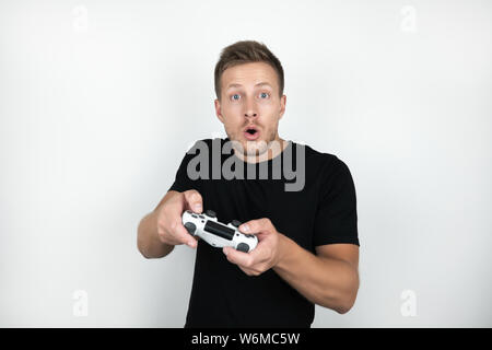 handsome young man wearing black t-shirt holding joystick in his hands plays video game isolated white background. Stock Photo