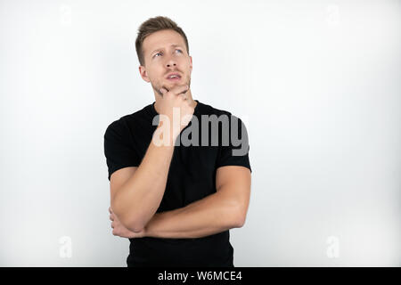 handsome young man wearing black t-shirt touching his face with one hand looks pensive isolated white background Stock Photo
