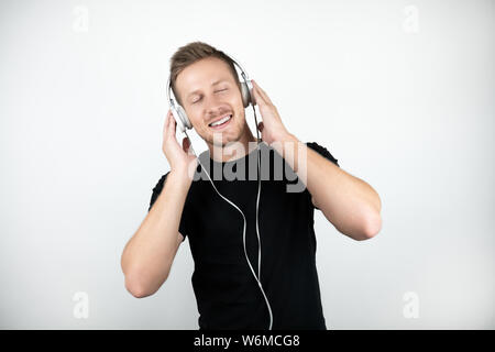 handsome young man wearing black t-shirt listening to music in headphones showing ok sign on isolated white background Stock Photo