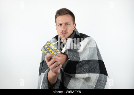 handsome young sick man wrapped checkered plaid holds pills on isolated white background Stock Photo