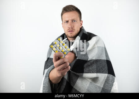 handsome young sick man wrapped checkered plaid holds pills and nasal spray on isolated white background Stock Photo