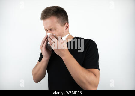 handsome young sick man blows his nose and holds nasal spray on isolated white background Stock Photo