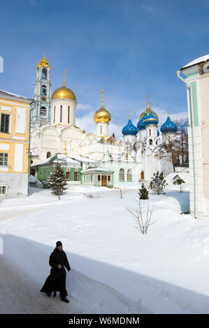 Orthodox monk walking on snow against a church. Trinity Lavra of St. Sergius, Russia Stock Photo