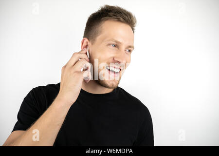 handsome young smiling man wearing black t-shirt having pleasant phone conversation using wireless headphones on isolated white background Stock Photo