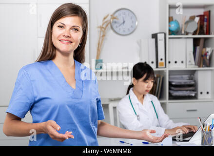 Portrait of young female doctor making welcome gesture welcoming patient to clinic Stock Photo