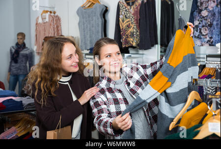 Two cheerful women shopping in clothing boutique and choosing warm cardigan Stock Photo