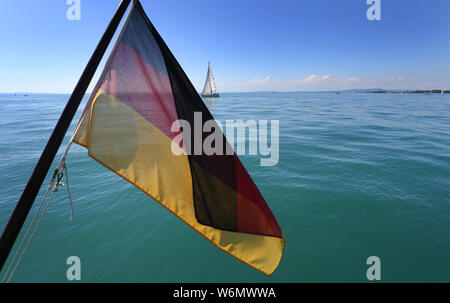 30 July 2019, Baden-Wuerttemberg, Langenargen: The German flag hangs from a ship in front of the blue water of Lake Constance. Photo: Karl-Josef Hildenbrand/dpa Stock Photo