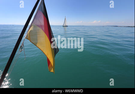 30 July 2019, Baden-Wuerttemberg, Langenargen: The German flag hangs from a ship in front of the blue water of Lake Constance. Photo: Karl-Josef Hildenbrand/dpa Stock Photo