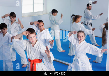 Group of young children doing karate kicks with male coach during karate class Stock Photo