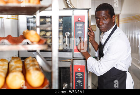 Experienced baker controlling process of baking bread, programming professional oven at bakery Stock Photo