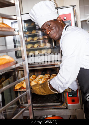 Portrait of African American baker controlling process of baking bread in professional oven at bakery Stock Photo