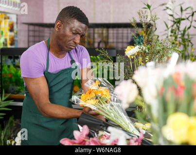 African American man owner of flower shop looking dissatisfied and worried with state of flowers Stock Photo