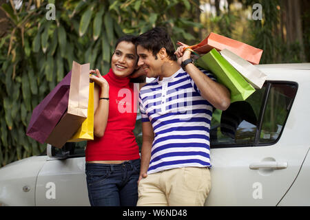 Couple leaning against a car with shopping bags Stock Photo