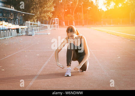 Young woman hands tie laces on her sport shoes on a stadium, ready for running Stock Photo
