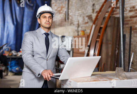 Male architect holding laptop and supervising process of building brick house Stock Photo