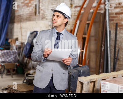 Male architect holding papers and supervising process of building brick house Stock Photo