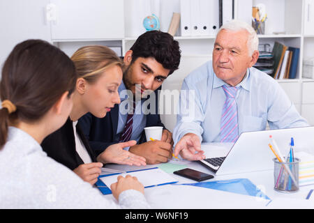 Managers are writing financial reports and discussing with mature boss in the office. Stock Photo