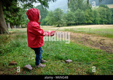 Full length view of a 3-4 year old girl playing outside in a rainy rural landscape in Germany wearing a red rain jacket Stock Photo