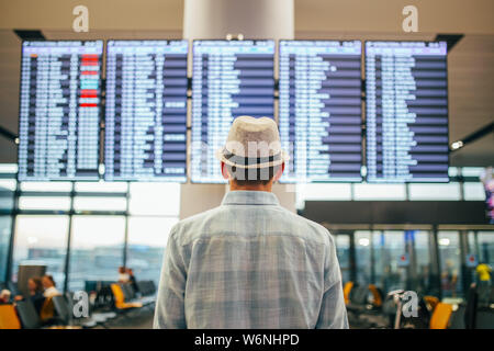 Solo traveler - man standing inside airport terminal looking at a schedule.  Travel and transportation themed image. Stock Photo