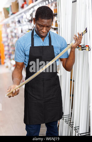 Confident satisfied  smiling African-American handyman choosing materials for overhauls in household store Stock Photo