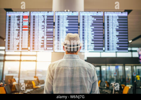 Solo traveler - man standing inside airport terminal looking at a schedule.  Travel and transportation themed image. Stock Photo