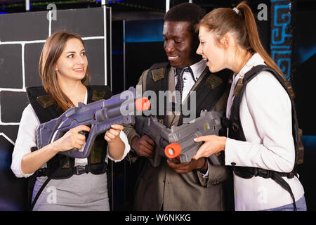 Smiling  positive associates – afro man and two European women posing at laser tag room Stock Photo