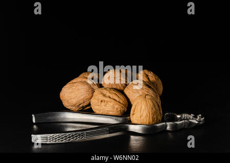 Walnuts with nutcracker over black background. Stock Photo