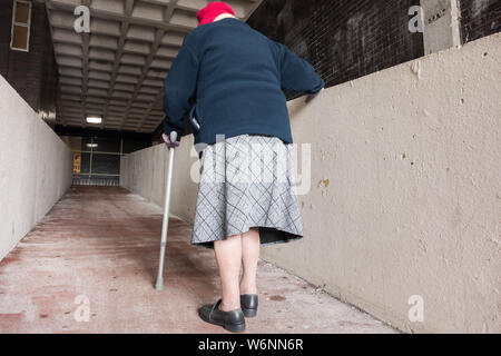 Rear view of 90 year old woman walking up ramp in shopping centre. UK Stock Photo