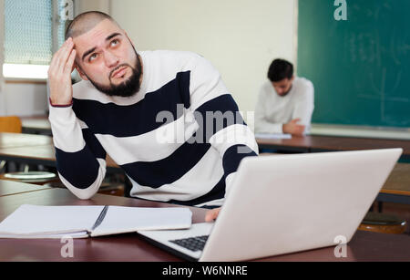 Young guy studying with laptop at desk in classroom Stock Photo
