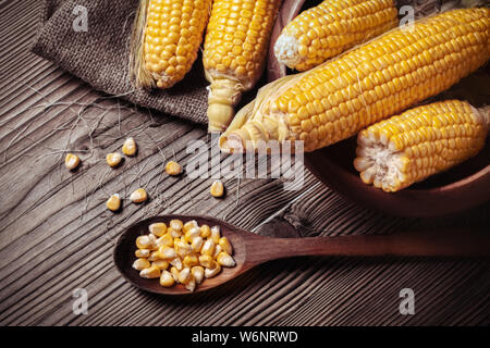 Bowl with corn fresh sweet organic corn seeds on wooden table. Maize on sackcloth.  Corn grains in wooden spoon on rustic wooden table in kitchen.  He Stock Photo