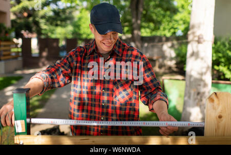 Man uses a tape measure to mark the length of a piece of lumber. Stock Photo