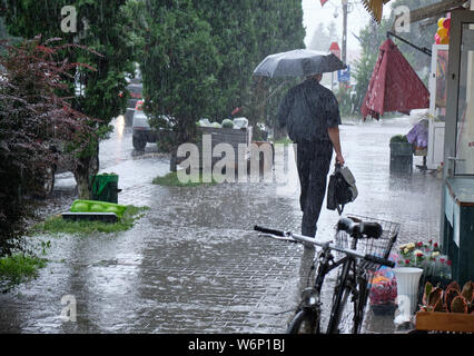 Man with briefcase walking in heavy rain with umbrella.  Rain creating massive puddles on sidewalk Stock Photo