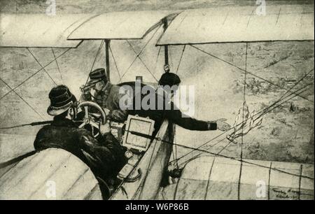 'The Fourth Arm in the Great War: French Air-scouts at work', First World War, 1914-1918, (c1920). 'A powerfully engined French biplane as used for detailed reconnaissance. The pilot is at his control-wheel: one of the two observers is studying the land below through his field-glasses, while the other is throwing earthward, over the French lines, and in a small tube, a written report as to what has been seen. This tube is visible as it falls, bright-coloured ribbons being attached to it, and when it is retrieved by the nearest troops, - who are warned to be on the look-out for such messages fr Stock Photo