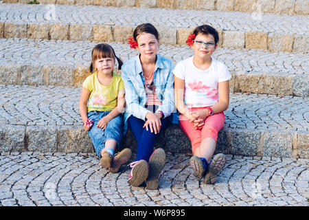 Three sisters sitting on stone stairs - during summer holidays Stock Photo