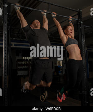 An athletic young couple is doing a fitness training together and having fun. Muscular man and woman are doing the exercise toes to bar. Stock Photo