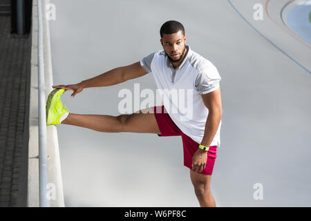 Concentrated African American sportsman stretching his right leg Stock Photo