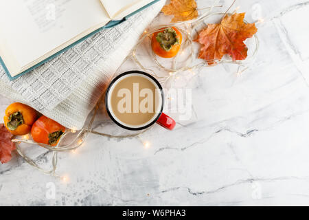 Enamelled red cup of coffee with milk, spices - book, persimmon, sweater, autumn maple on light background Stock Photo