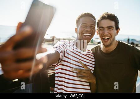 Two smiling young men taking selfie while standing by a car outdoors. Friends making a self portrait outdoors on a summer day. Stock Photo